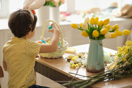 child boy wearing bunny ears sitting in the kitchen at the table. child holding painted eggs...