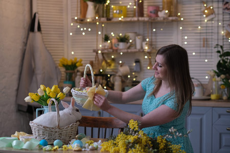 young woman decorates Easter basket in cozy kitchen interior. table kitchen with flowers, easter...
