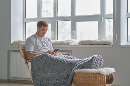 Young man relaxing on cozy rocking-chair in light room. Joy of life. Total relaxation.の写真素材