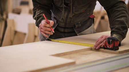 Close up. Carpenter holding a measure tape on the work bench. Woodwork and furniture making concept. Carpenter in the workshop marks out and assembles parts of the furniture cabinetの写真素材