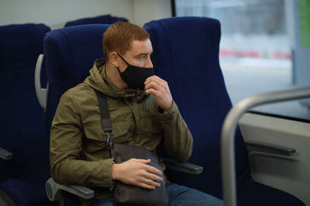 Handsome guy in respirator use a smartphone and keep social distancing to crowd while commuting in the metro or train. Infection and air pollution prevention conceptの写真素材