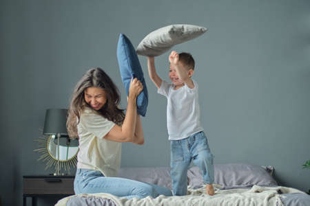 mother playing with her toddler little son on a bed together. Family moments, children care. Motherhood, maternity leave conceptの写真素材