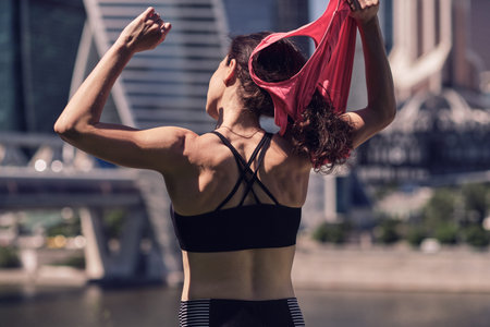 Rear view of middle age womans takes off her jersey after an intense workout and looking at a view....