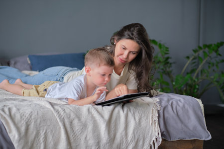 mother and son with tablet at home. Mother showing media content on line to her son in a tablet in the living room in a house interiorの写真素材