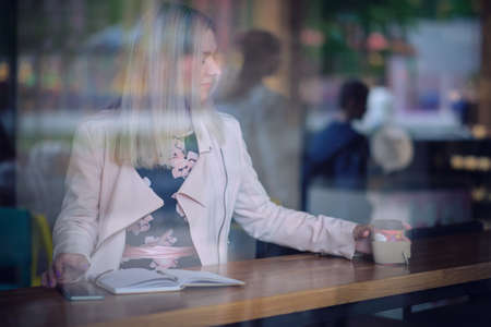 woman in the cafe sits at a table, drinks coffee and looking away. vintage color toneの写真素材