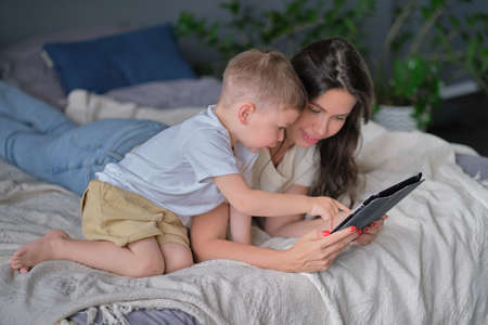 mother and son with tablet at home. Mother showing media content on line to her son in a tablet in the living room in a house interiorの写真素材