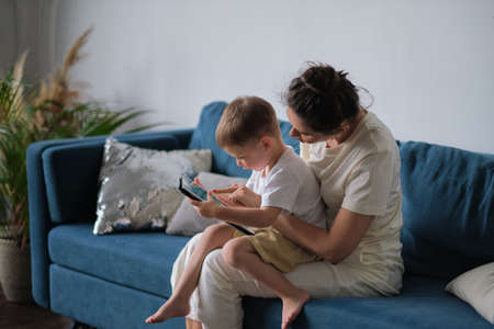 mother and son with tablet at home. Mother showing media content on line to her son in a tablet sitting on a couch in the living room in a house interiorの写真素材