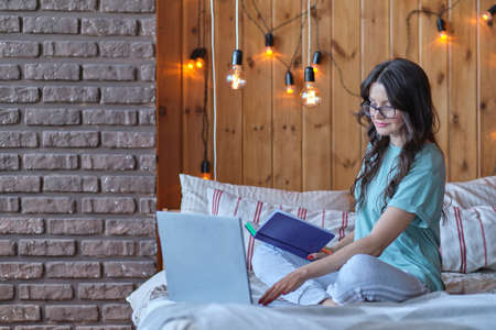 beautiful woman is sitting on the bed and working on a laptop.の写真素材