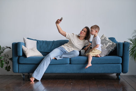 Mother taking a selfie with her son sitting on a couch in the living room at home