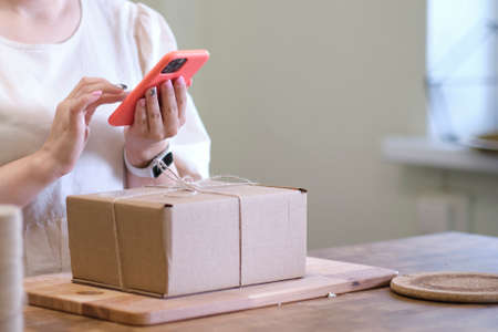 Small business owner standing at her shop arranges delivery through the application on a smartphone. online store seller entrepreneur packing package post shipping box preparing delivery parcel.の写真素材