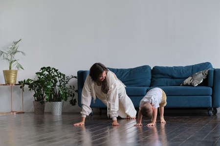 Happy mindful single mother doing morning exercises in yoga pose with kid playing at home. morning exercises in pajamas. child interferes with the workoutの写真素材
