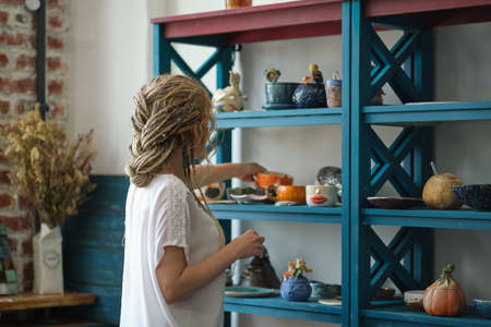 hostess of the ceramic workshop lays out her ceramic dishes on the shelves. feng shui concept. Small business officeの写真素材
