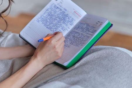 lifestyle soft image of unrecognizable young woman sitting on her cozy bed and making notes to her diary. Fall season mood.の写真素材