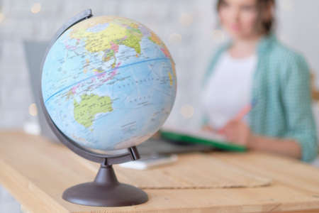 blurred globe in the foreground. in the background a woman works at a laptop, illustration of an international company or online profession. freelancer works remotelyの写真素材