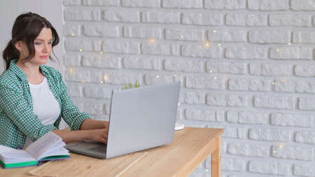 woman sitting at a table working at a laptop computer. concept of remote work from home. home office in the kitchen. professional freelancerの写真素材