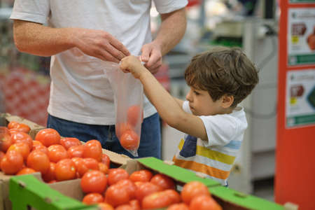 Little boy with Dad choosing tomatoes food in fruit vegetable shopping storeの写真素材