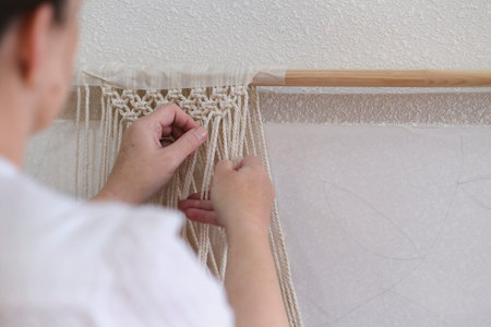 base knots of macrame, the view from behind the shoulder close-up of the women hands, she ties knots. ECO friendly modern knitting DIY natural decoration concept.の写真素材