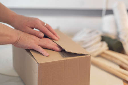 woman entrepreneur packs a handmade product in a cardboard box. delivery of goods for a small business. an elderly woman earns her hobby from home.の写真素材