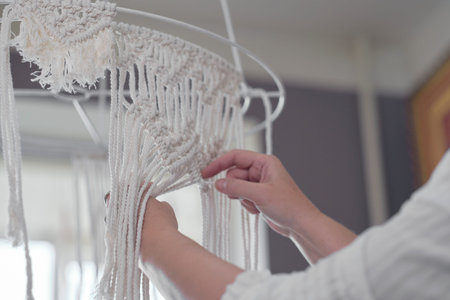 woman working on custom macrame decor with tools over a creative desktop watched from above. Hobby...