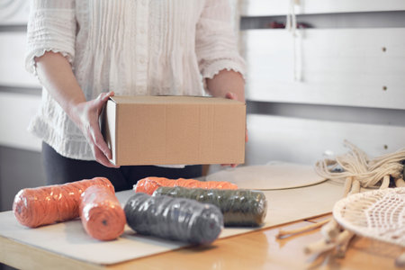 woman entrepreneur packs a handmade product in a cardboard box. delivery of goods for a small business. an elderly woman earns her hobby from home.の写真素材