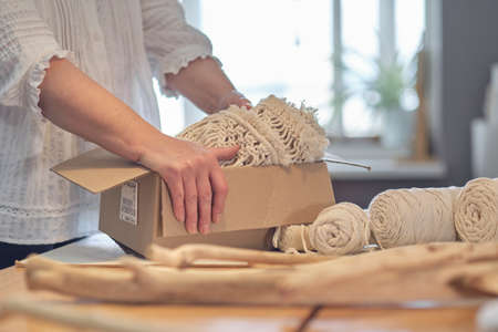 woman entrepreneur packs a handmade product in a cardboard box. delivery of goods for a small business. an elderly woman earns her hobby from home.の写真素材