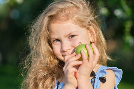 Little girl smiles at the camera. pretty girl posing for a photo and holding two green fresh apples in her handsの写真素材