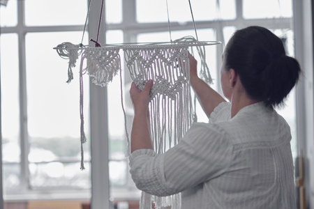 woman working on custom macrame decor with tools over a creative desktop watched from above. Hobby...