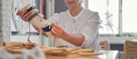 woman working on custom macrame decor with tools over a creative desktop watched from above. Hobby...