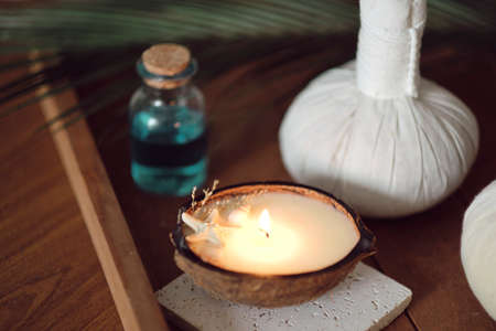 candle with the scent of coconut on a wooden table. Beautiful tropical spa concept. Cotton pouches with herbs for massage on wood background with green leafs. Herbal compress ballsの写真素材