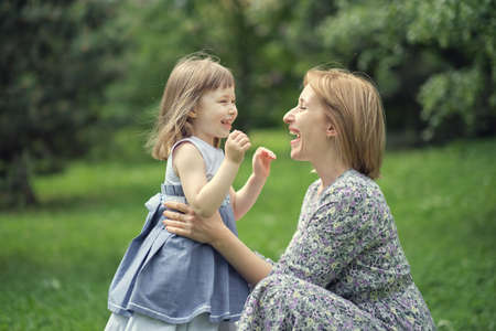 Little cute girl with her mother on the walk. Mother with child girl playing in garden. Woman with daughter huging and having fun outdoors.の写真素材