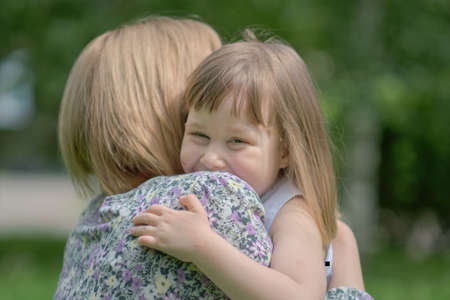 Side view close up head shot happy cute daughter hugging embracing cuddling mother. Concept of happy family. Portrait happy smiling child hugging mother in summer dayの写真素材