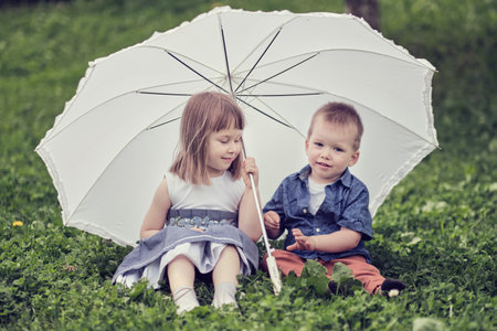 little girl and boy are hiding under an umbrella. brother and sister are playing in the park.の写真素材