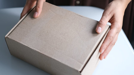 woman opening parcel indoors. woman opening and unpacking cardboard box parcel in living room at...
