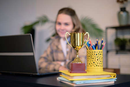 pretty teen girl with laptop and trophy on the table. little girl with a cup. Girl winner. little girl won the competition.の写真素材