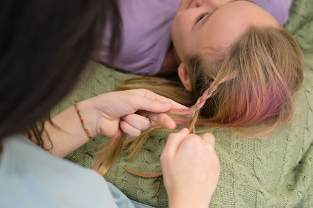 girl makes a braid to her friend. Hair weaving hairstyles. Girlfriend braids her hands with...