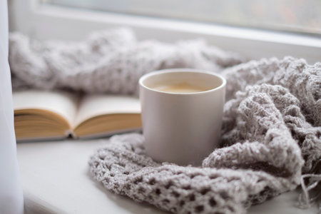 Cozy home with cup of coffee and a book. Hygge style. Mug of black coffee wrapped in warm scarf on wooden board. Top view, vintage style, Still life.の写真素材