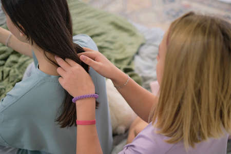 girl makes a braid to her friend. Hair weaving hairstyles. Girlfriend braids her hands with ringlets. Two young multinational girls spending time together, pajama party.の写真素材