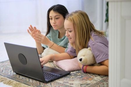 two teenage girls lie on the bedroom floor and watch a movie on a laptop. Friendship concept