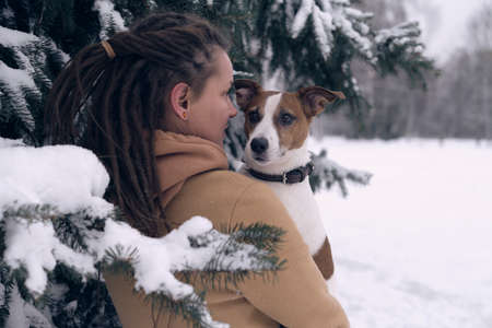 playful woman with dog. stylish hipster woman hugging and smiling cute puppy in snowy cold winter park. moments of true happiness.の写真素材