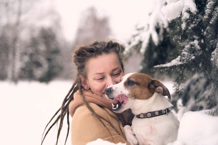 playful woman with dog. stylish hipster woman hugging and smiling cute puppy in snowy cold winter park. moments of true happiness.の写真素材