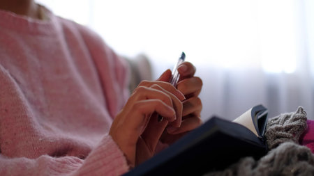 unrecognizable woman in warm knitted sweater writes down plans or tasks for the new year.