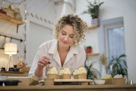 confectioner squeezes out a white cream in the form of roses flowers. process of decorating cupcakes with white whipped cream. Decorating a white cake with cream from the pastry bag.の写真素材
