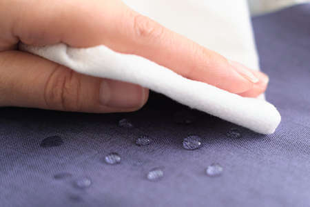 hand wipes drops of water from a cloth. Water drops on waterproof textile material. short depth of field. Waterproof fabric on sofa.の写真素材