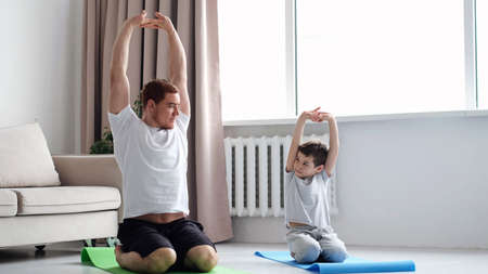 Father and Son do Spotting. Sport at Home. Warm Up in Quarter. Lying on Gymnastic Mat. Doing Sports. Man and Boy Train at Home.の写真素材