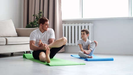 Father and Son do Spotting. Sport at Home. Warm Up in Quarter. Lying on Gymnastic Mat. Doing Sports. Man and Boy Train at Home.の写真素材