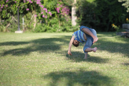 Mischievous preschooler boy somersaults on sand grass in the park.の写真素材