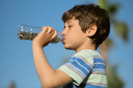 boy drinks water from plastic bottle. asian child drinking fresh water outdoors