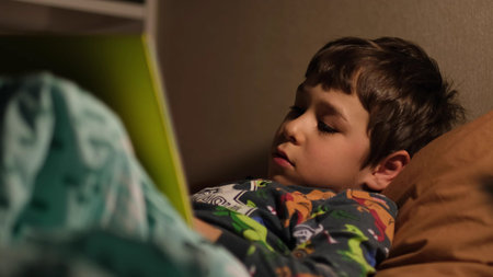 handsome boy read book with lamp before sleep. elementary school student reading a book before going...
