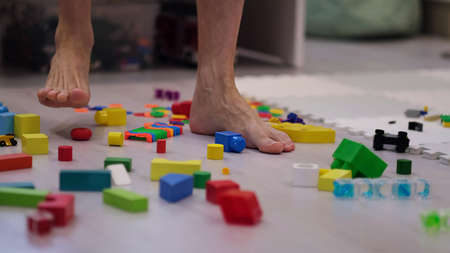 barefoot man walks among the scattered toys. Foot stepping on childrens toys. Scattered toys on the floor. concept of an abundance of toys in the modern world.の写真素材