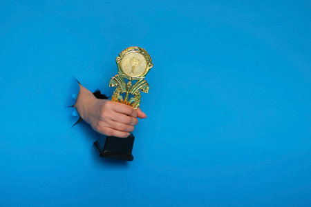 image of trophy in hand, concept for winning or success. Golden trophy on blue background, top view with space for textの写真素材